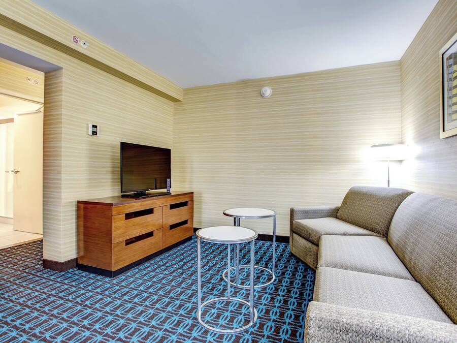 Hotelkamer met een bank, twee kleine tafels, een televisie op een houten kast en een kamerbreed tapijt met een patroon.