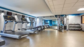 Ein Fitnessstudio mit Laufbändern, Kraftgeräten und einer Spiegelwand.