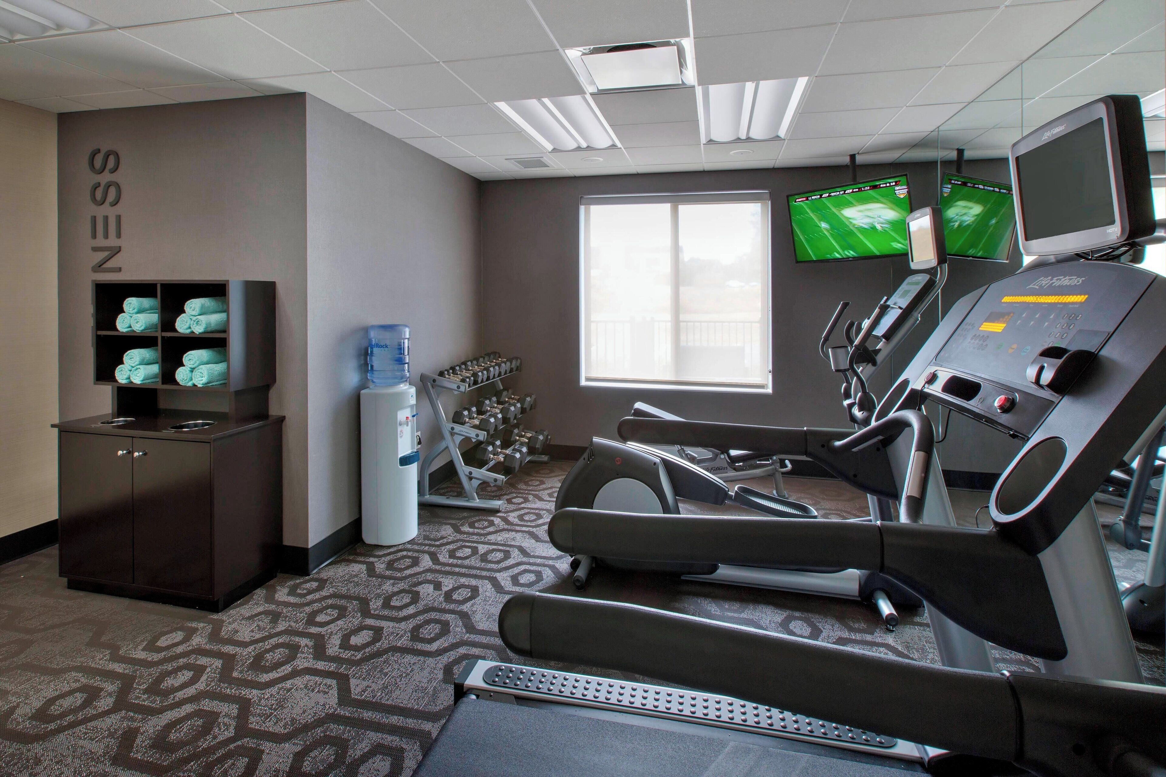 A gym with exercise equipment, a water cooler, and a TV on the wall.