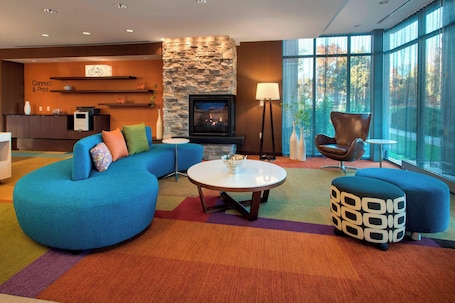A modern living room with a stone fireplace, a blue sofa, a round coffee table, and a large window with a view of trees.