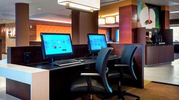 A modern reception desk with two computer monitors, a coffee machine, and a seating area with chairs.
