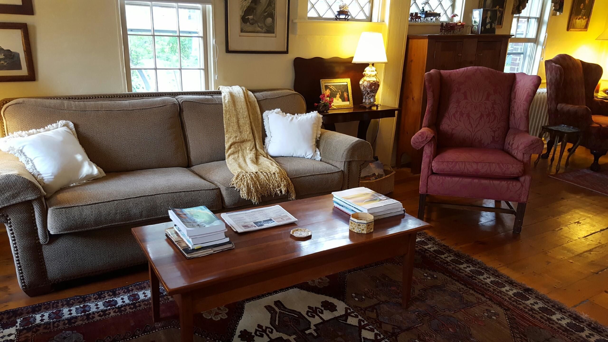 A cozy living room with a brown sofa, a red armchair, a wooden coffee table, and a patterned rug.
