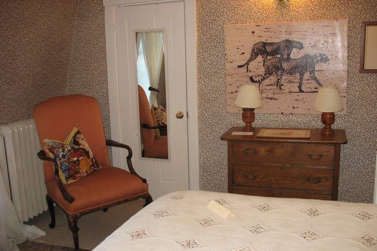 A bedroom with a bed, a chair, a dresser, a mirror, and a painting on the wall.