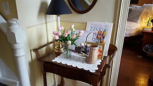 A small wooden table with a lace doily, a vase of pink tulips, a travel guide, and a wicker basket. - The 1720 House (Vineyard Haven)