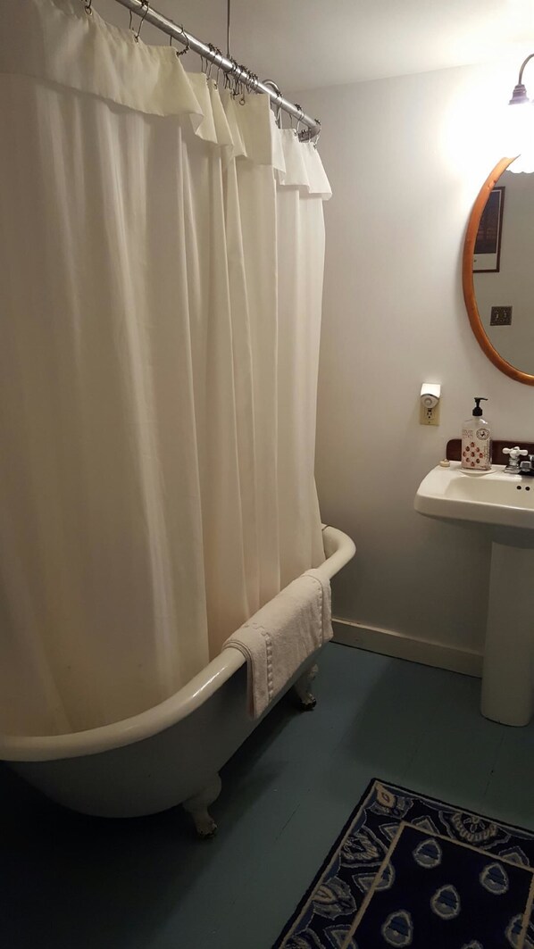Un baño con una bañera de patas de león, un lavamanos blanco y una cortina de ducha.