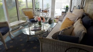 A sunlit room with wicker furniture, a glass coffee table, and a view of the outdoors. - The 1720 House (Vineyard Haven)