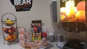Una preparación para el desayuno con dispensador de jugo de frutas, frutero y diversos alimentos envasados.