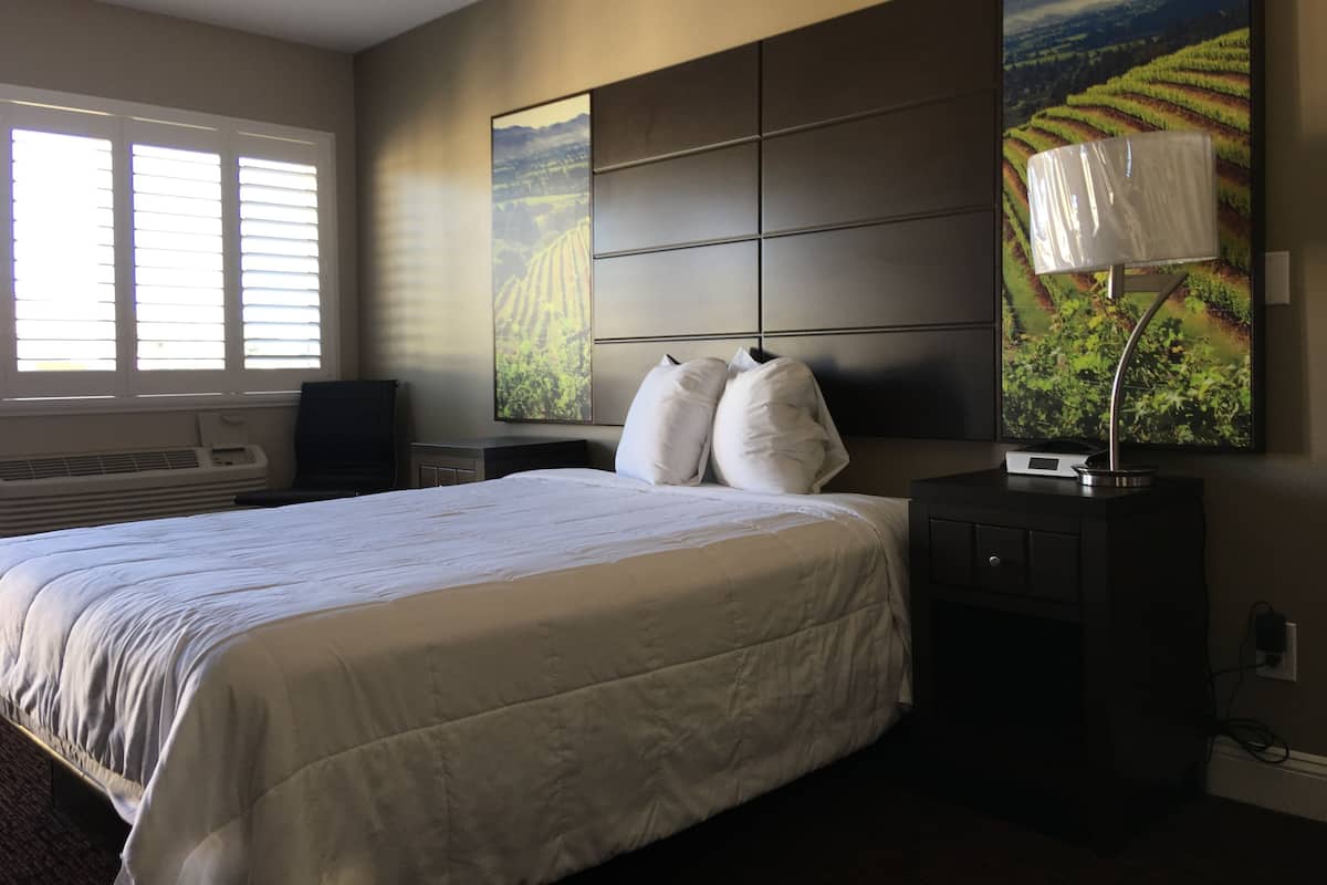 A hotel room with a large bed, a flat-screen TV, a desk with a lamp, and two paintings on the wall.