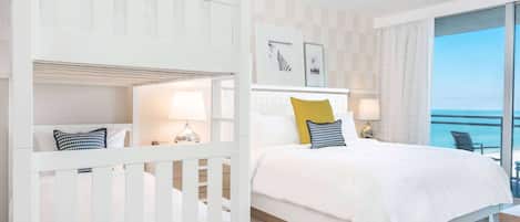 A hotel room with a bed, a crib, a balcony with a view of the sea, and a small table with a lamp.