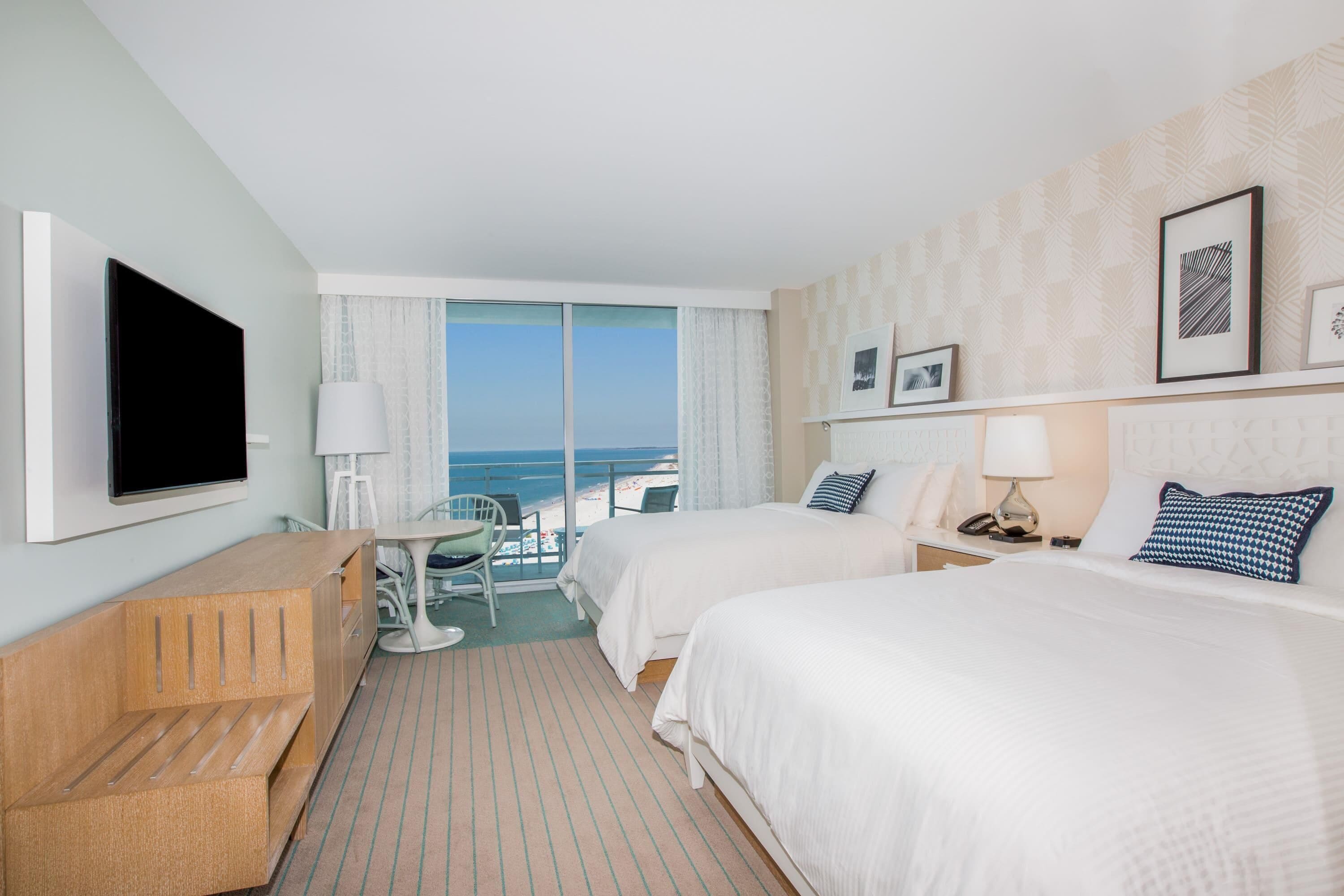 Une chambre d’hôtel avec deux lits, un bureau, une télévision et une vue sur l’océan.