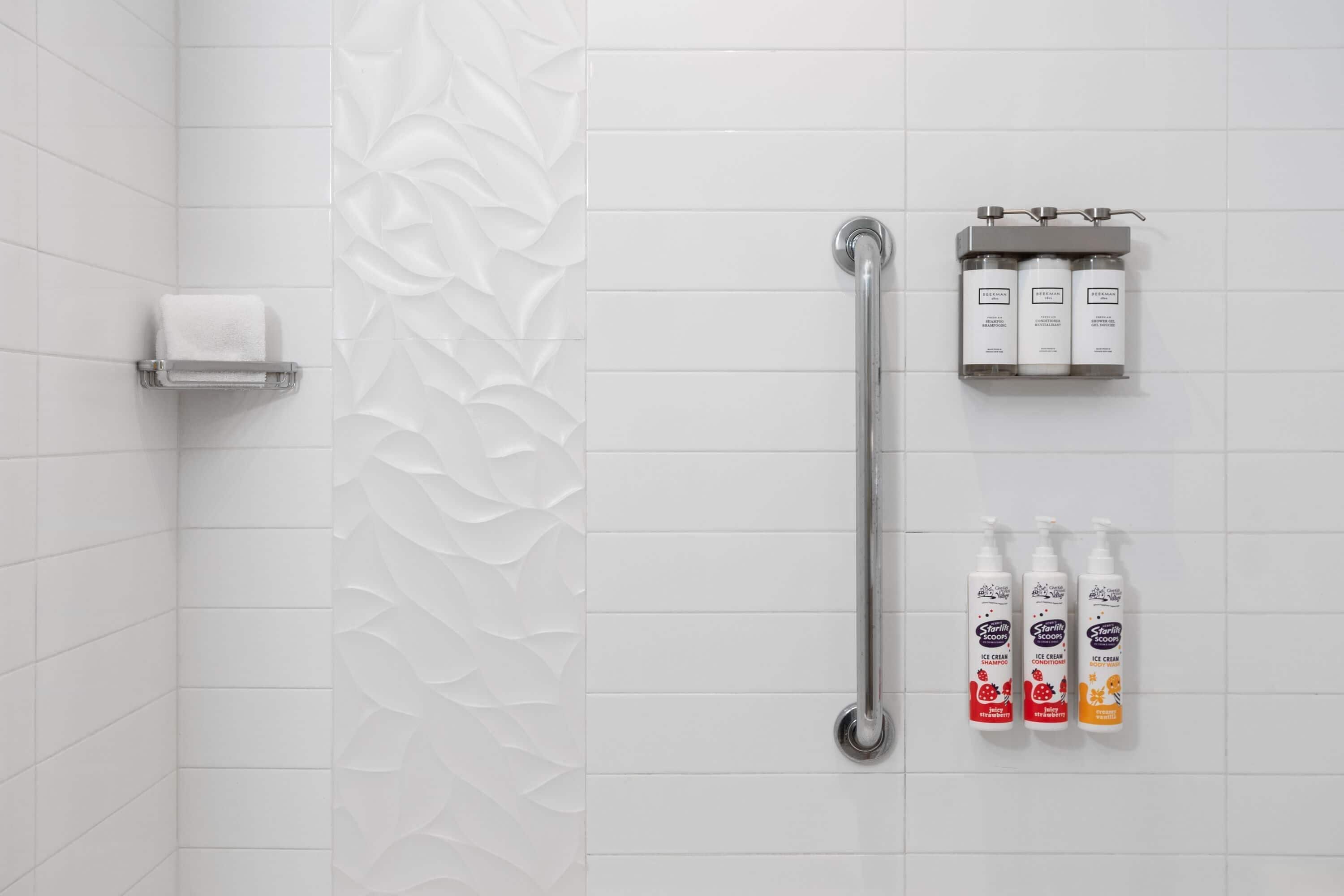 Een badkamer met witte tegels, een handdoekhouder, een handgreep en drie flessen shampoo.