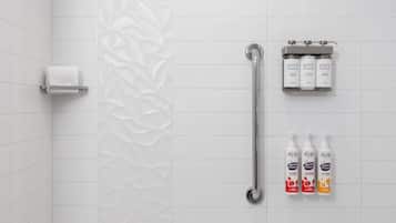 Un baño con azulejos blancos, un perchero, una barra de apoyo y tres botellas de champú.
