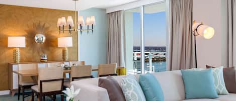 A hotel room with a dining area, a sofa with patterned cushions, a large mirror, and a view of the city.