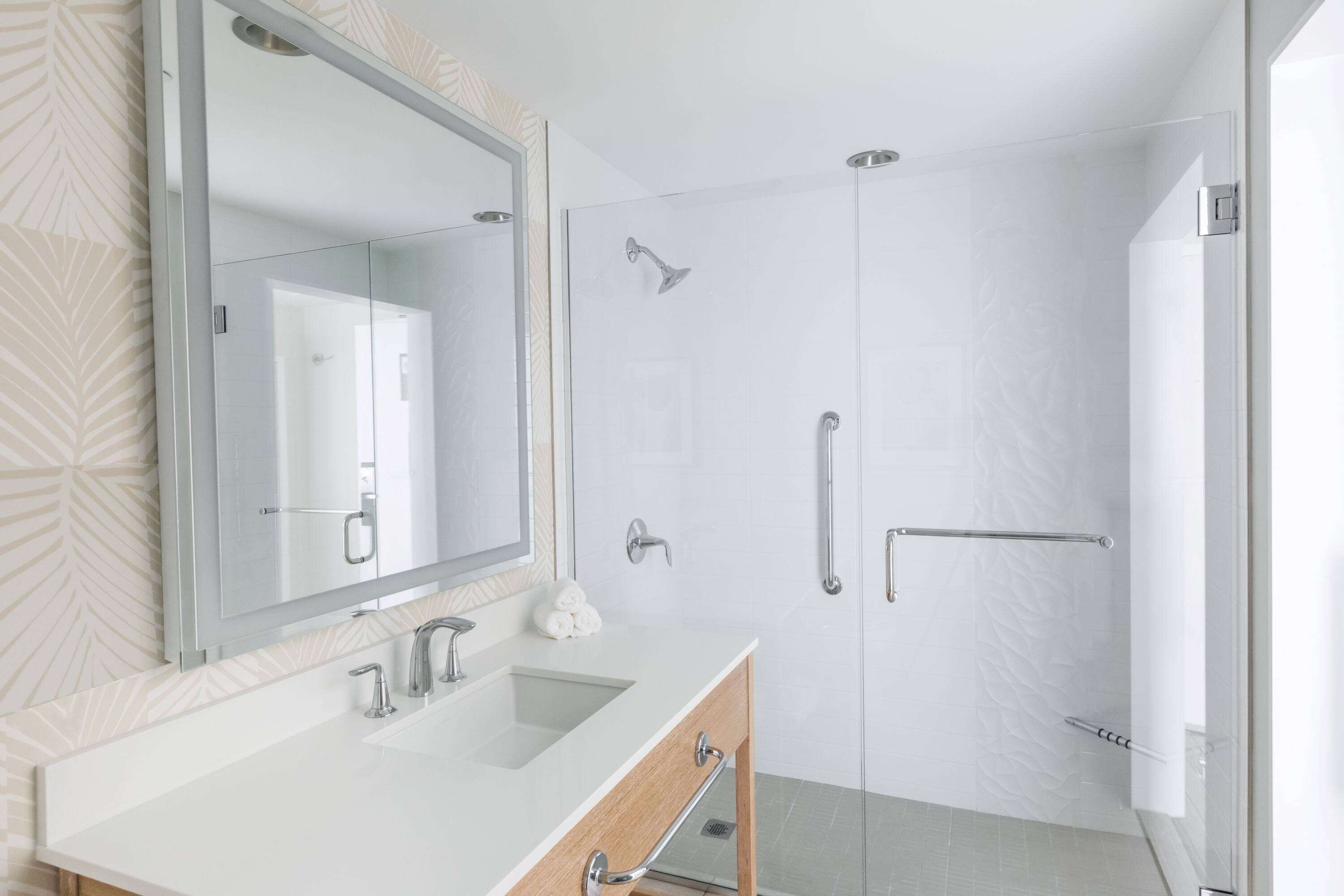Un baño moderno con tocador doble, un espejo grande y una ducha a ras de suelo con puerta de vidrio.