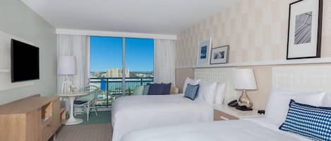 Habitación de hotel con dos camas, un escritorio, una silla, un televisor y ventana con vista a la ciudad.