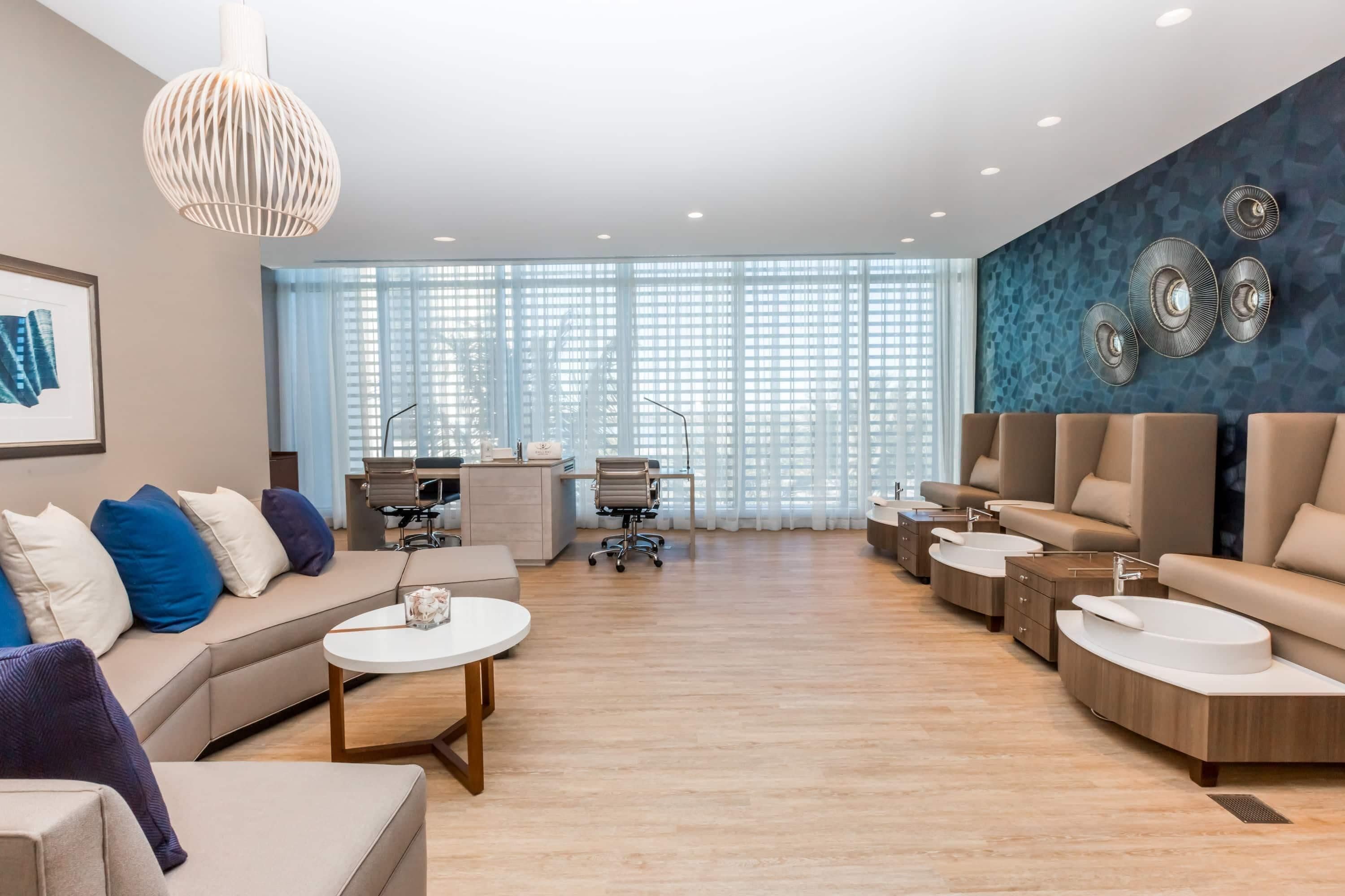 A modern hotel lobby with a sofa, armchairs, a desk, and a large window with blinds.