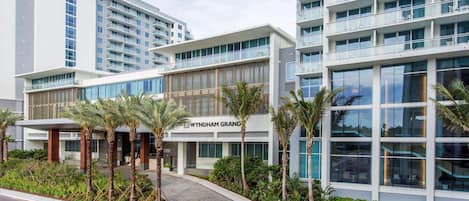 Un hotel moderno con una entrada destacada, varios pisos y un área exterior bien cuidada con palmeras.