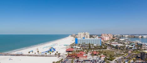 A coastal hotel with a beach view, parking lot, and a boardwalk with umbrellas.