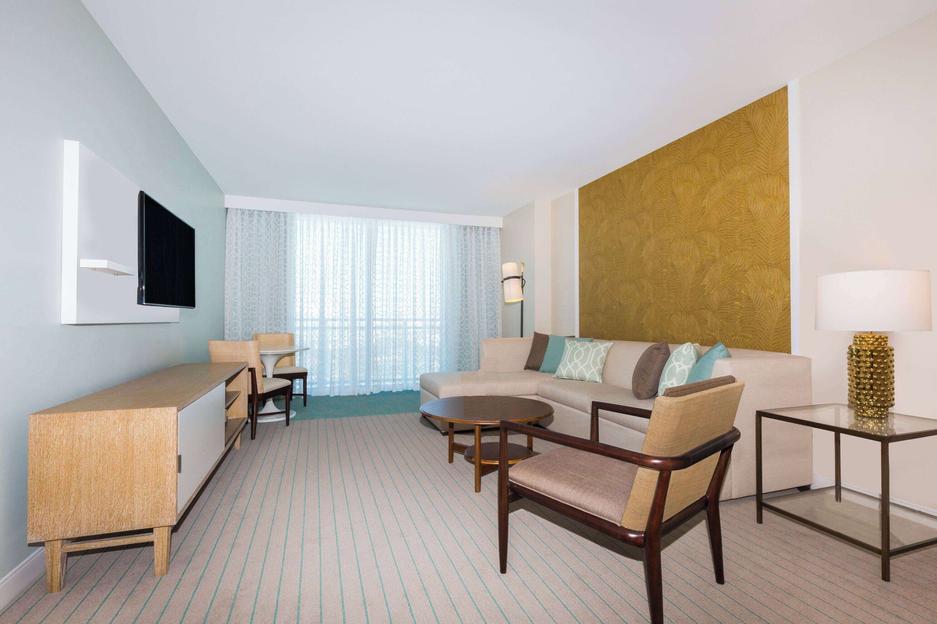 A hotel room with a sofa, armchair, small table, and a TV mounted on the wall.
