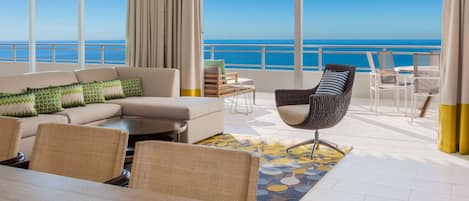 A spacious balcony with a clear view of the ocean, furnished with a sofa, chairs, and a dining table.