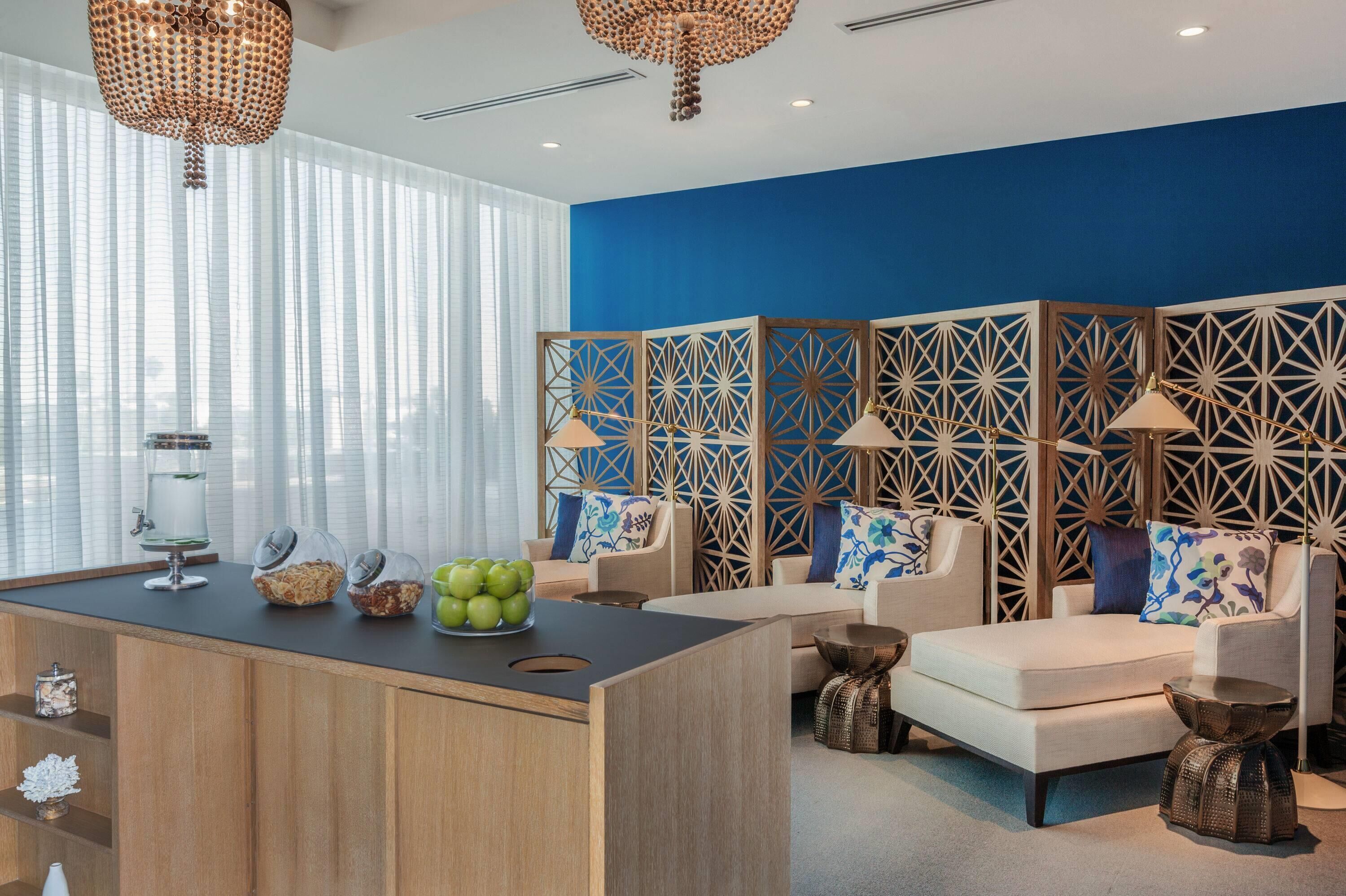 A modern hotel lobby with a blue accent wall, a reception desk, seating area, decorative panels, and a water dispenser.