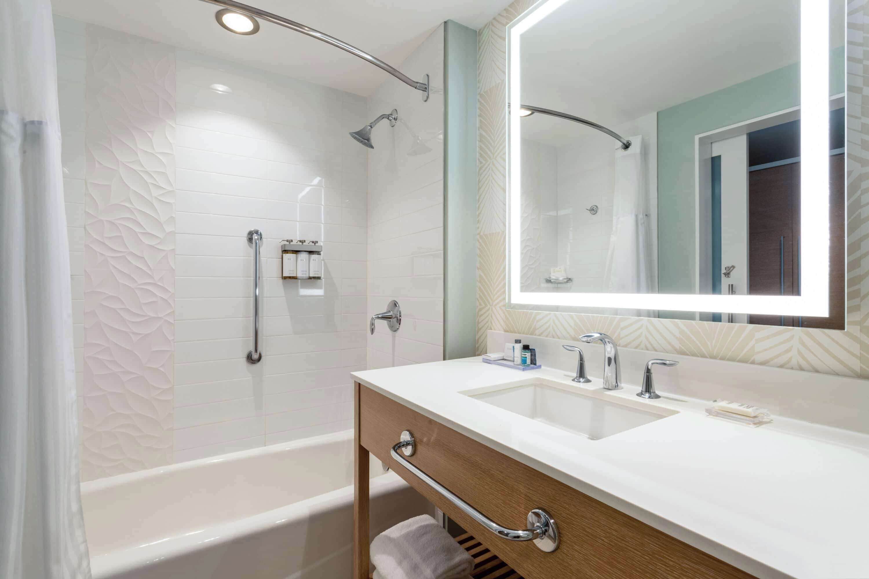 Ein modernes Badezimmer mit Badewanne, Waschtisch inklusive Spiegel und Duschbereich.