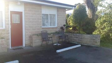 A motel with a brick exterior, a red door, and a small patio with two metal chairs and a table.