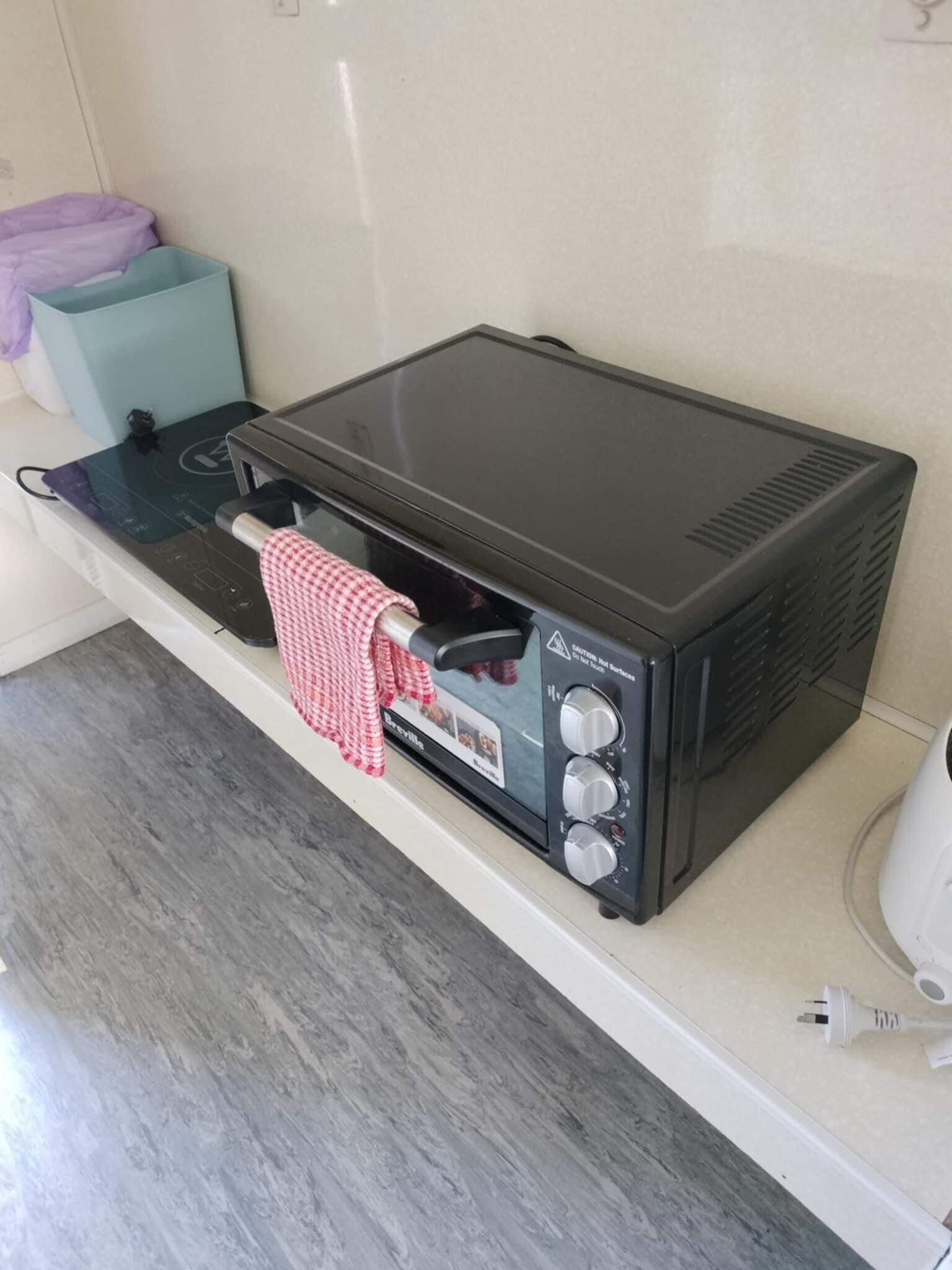 A kitchenette with a black induction cooktop, a red and white checkered towel, and a Breville oven.