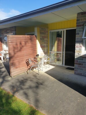 A patio area with a table and chairs, a sliding glass door, and a brick wall. - Otaki Motel (Otaki)