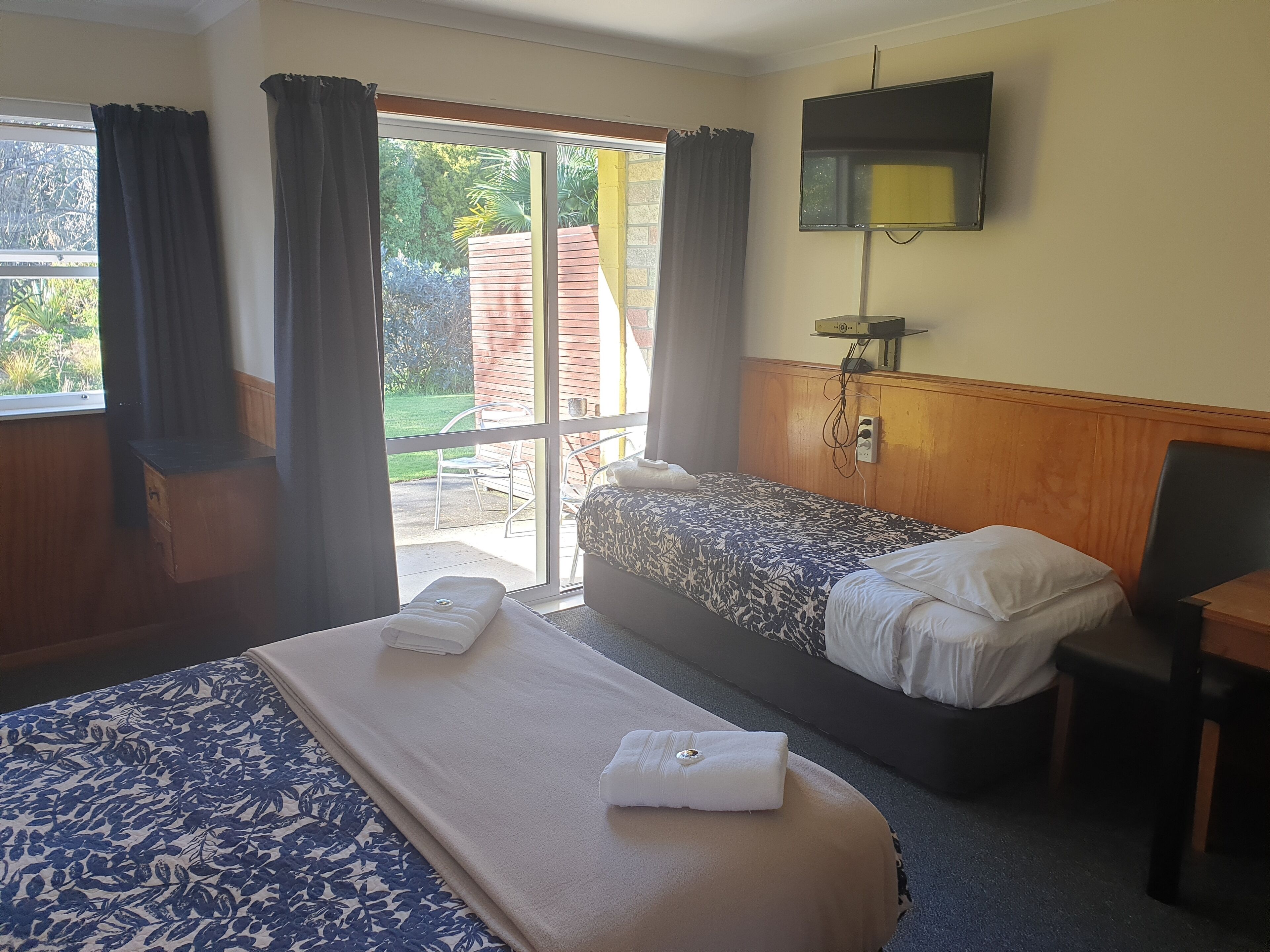 Quarto de hotel com duas camas, televisão fixada na parede e janela com cortinas.