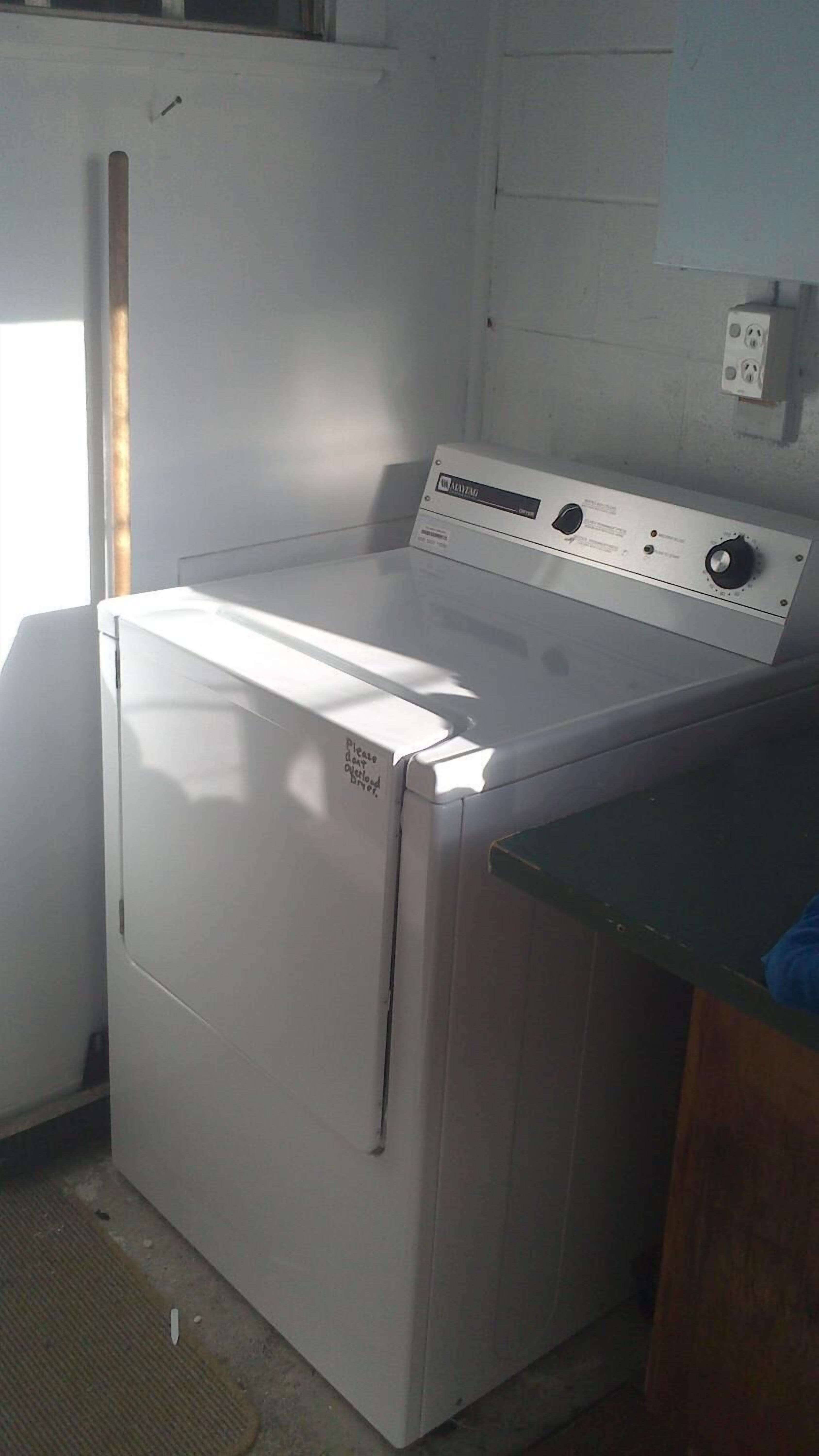 A compact, white front-loading washing machine in a small laundry room with a wooden counter and a power outlet on the wall.