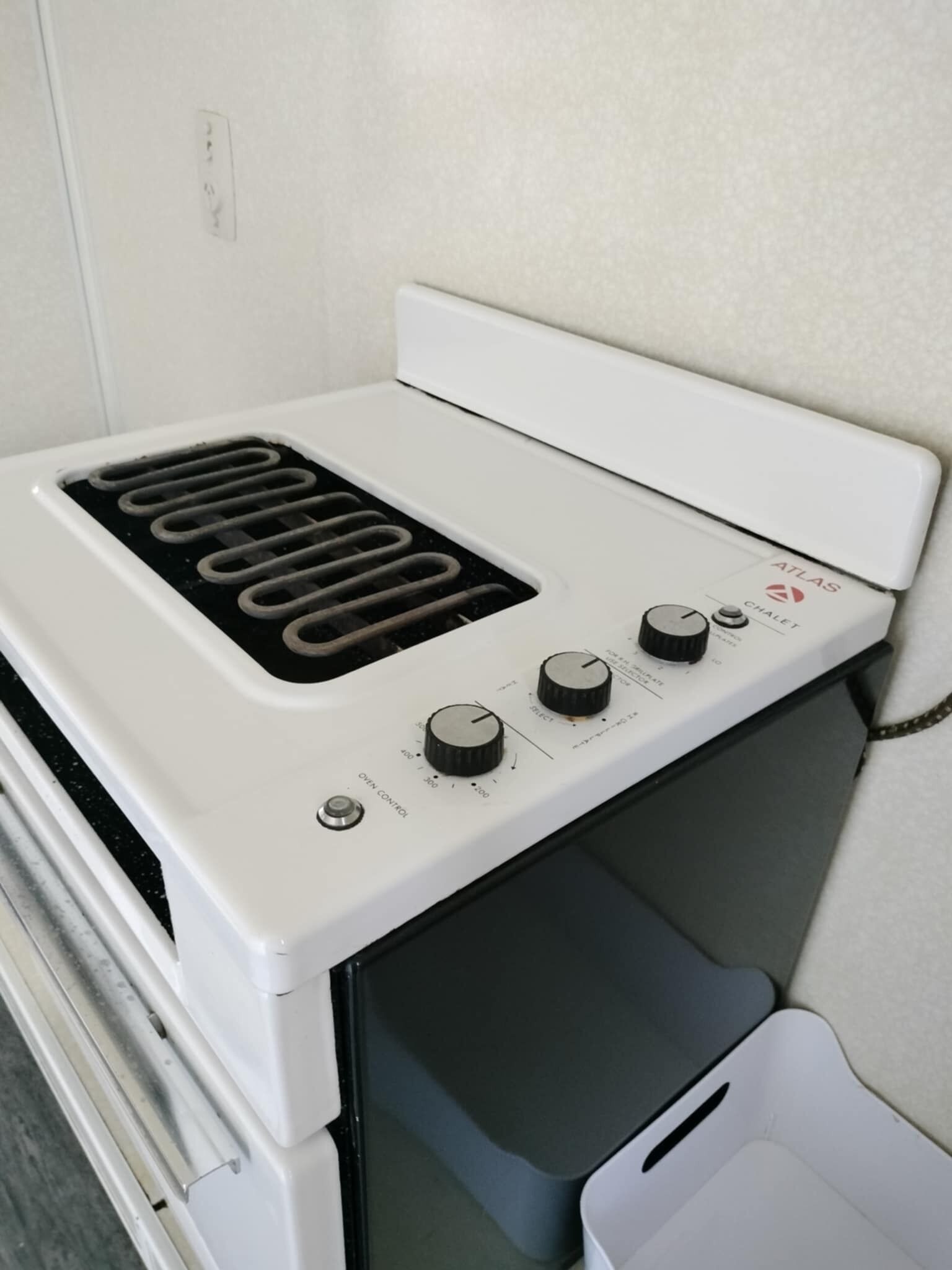 A white electric stove with a control panel, including knobs and a dial, in a kitchen setting.