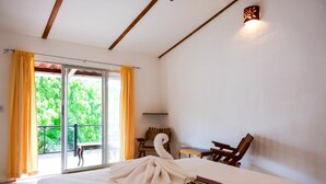 Hotelkamer met een bed, een handdoek in de vorm van een zwaan, een houten stoel, een klein tafeltje en een balkon met gele gordijnen.