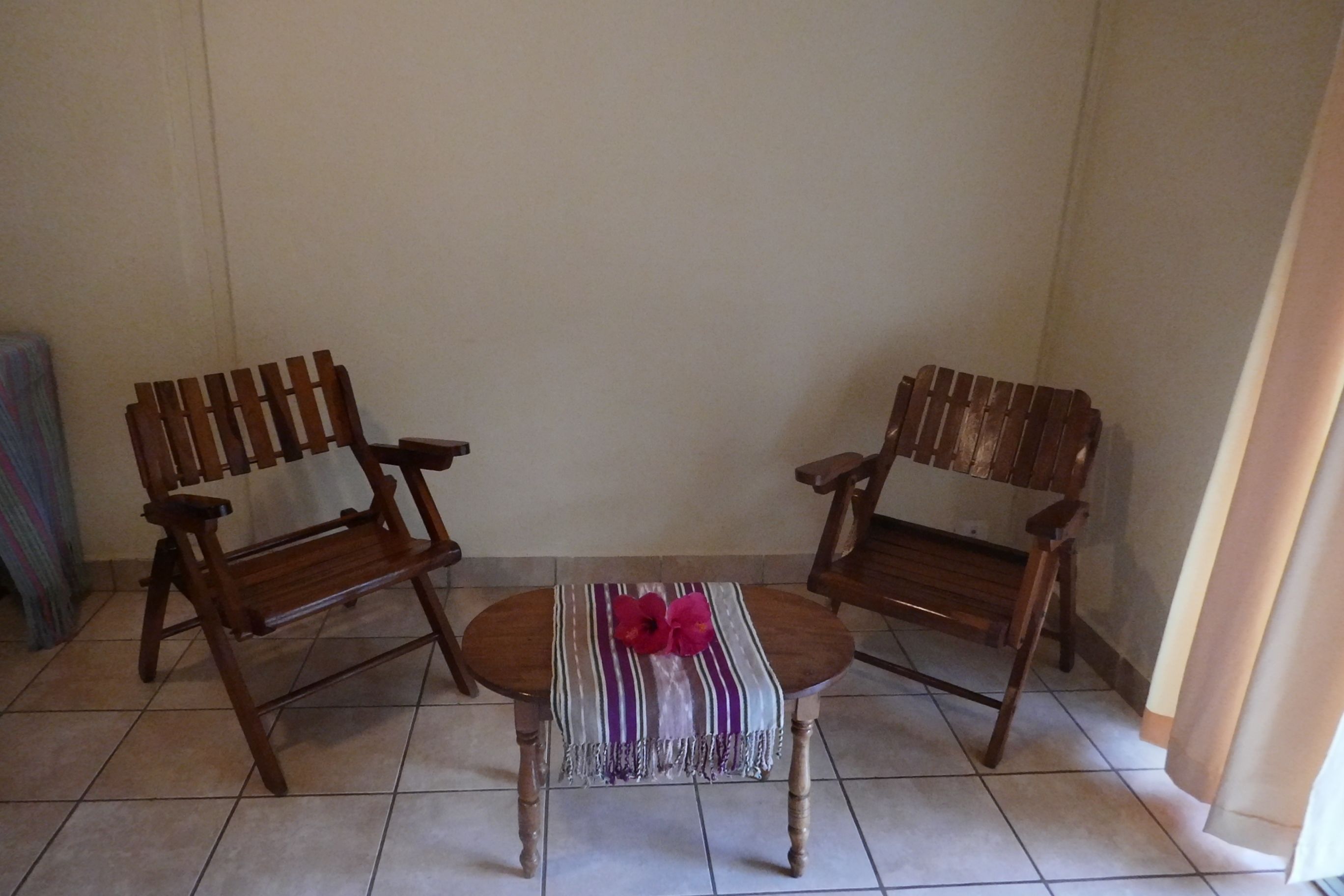 Een hoekkamer met twee houten stoelen en een tafeltje, een geruit tafelkleed en een roze bloem.