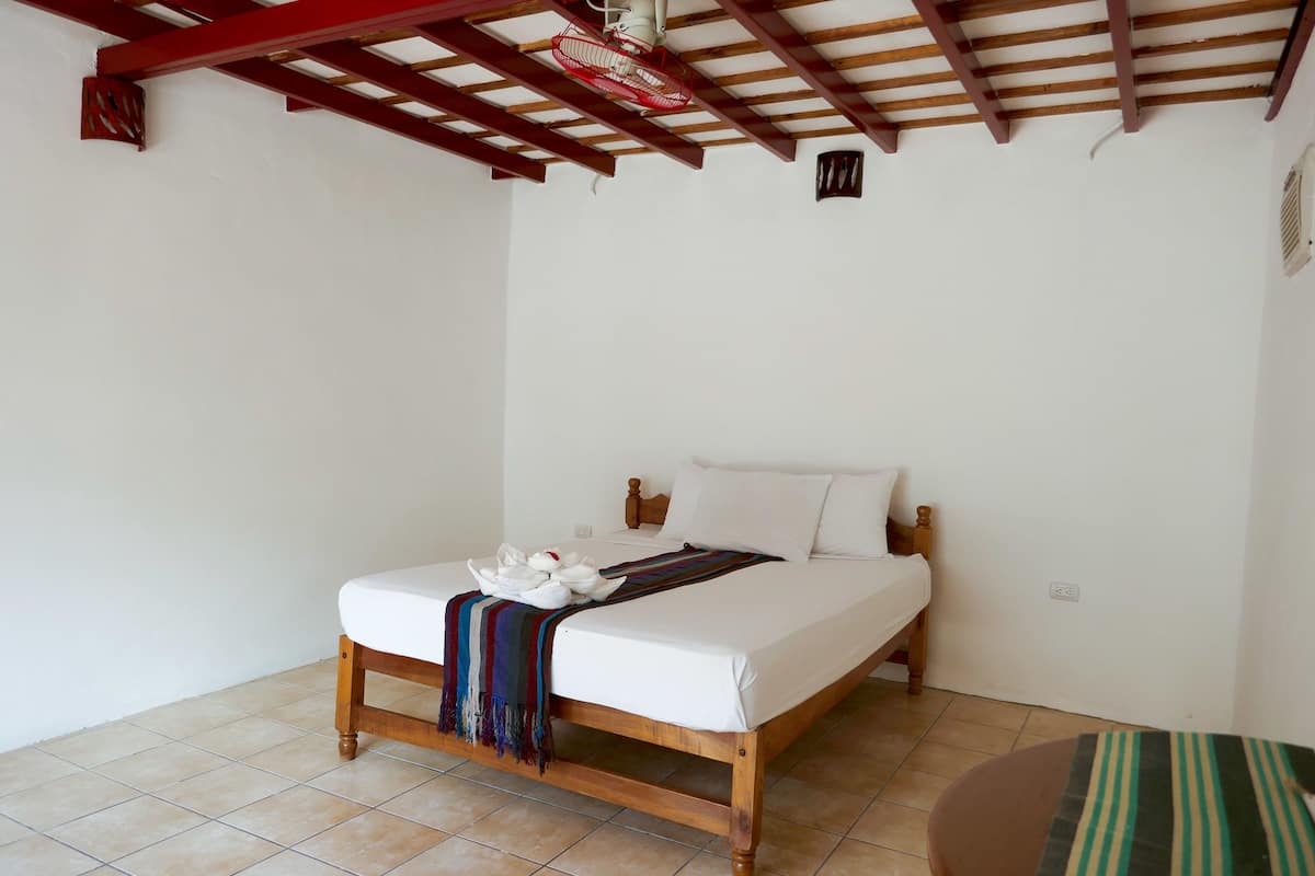 A single bed with a wooden frame, white bedding, and a colorful throw blanket.