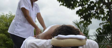 Sesión de masoterapia al aire libre, con un cliente recostado en una camilla y un terapeuta atendiendo.