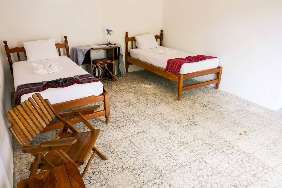 A room with two wooden beds, a wooden chair, and a small desk with a lamp.
