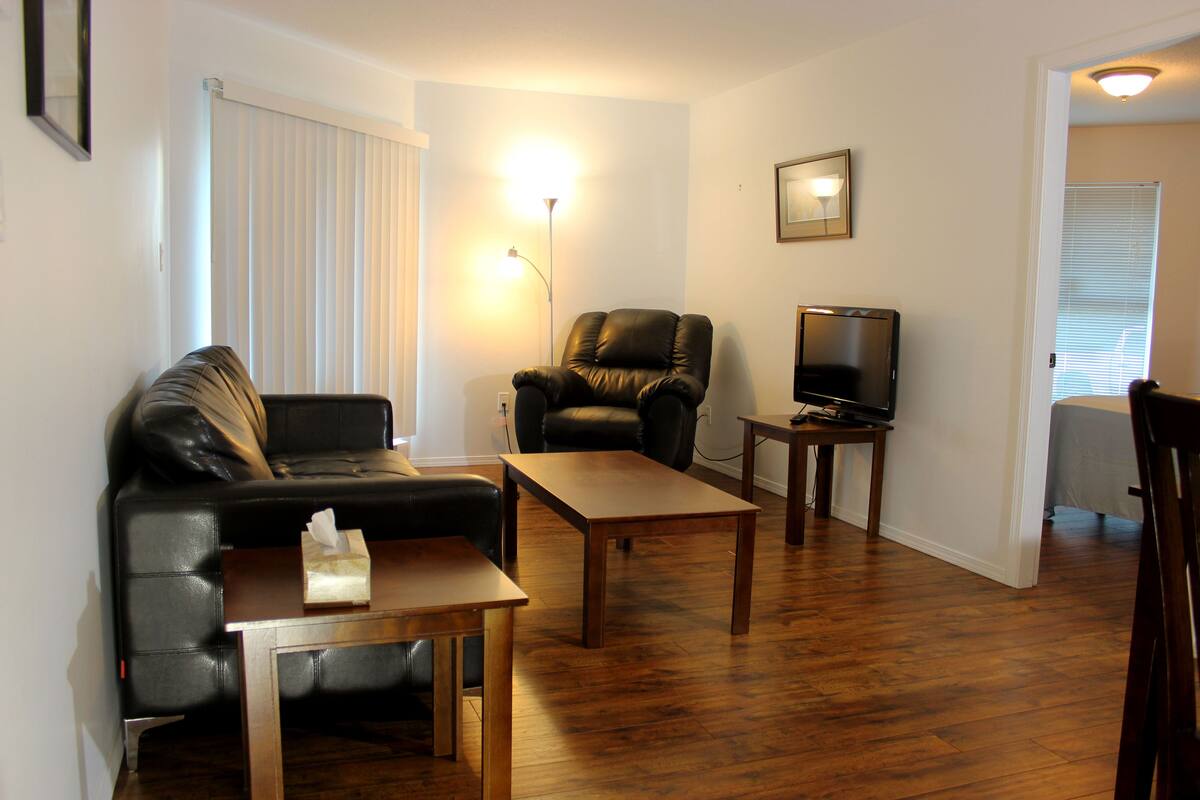 Ein Wohnzimmer mit einer Ledersofa, einem Holztisch, einem Ledersessel, einem Fernseher auf einem Holzgestell und einer Wandleuchte.