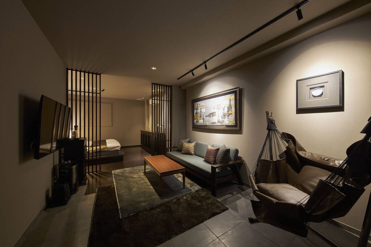 Un salon moderne avec un canapé, une table basse et un fauteuil suspendu. Un tableau orne le mur et un téléviseur y est fixé.