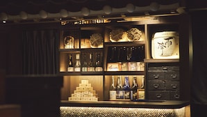 A bar area with shelves of bottles and boxes, a display of folded items, and a decorative ceiling. - SAKE Kura Hotel Kawasaki Shuku (Kawasaki)