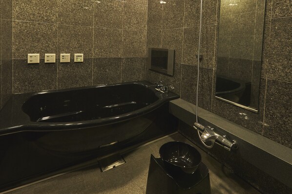 Een moderne badkamer met een zwart bad, een spiegel en een bedieningspaneel aan de muur.
