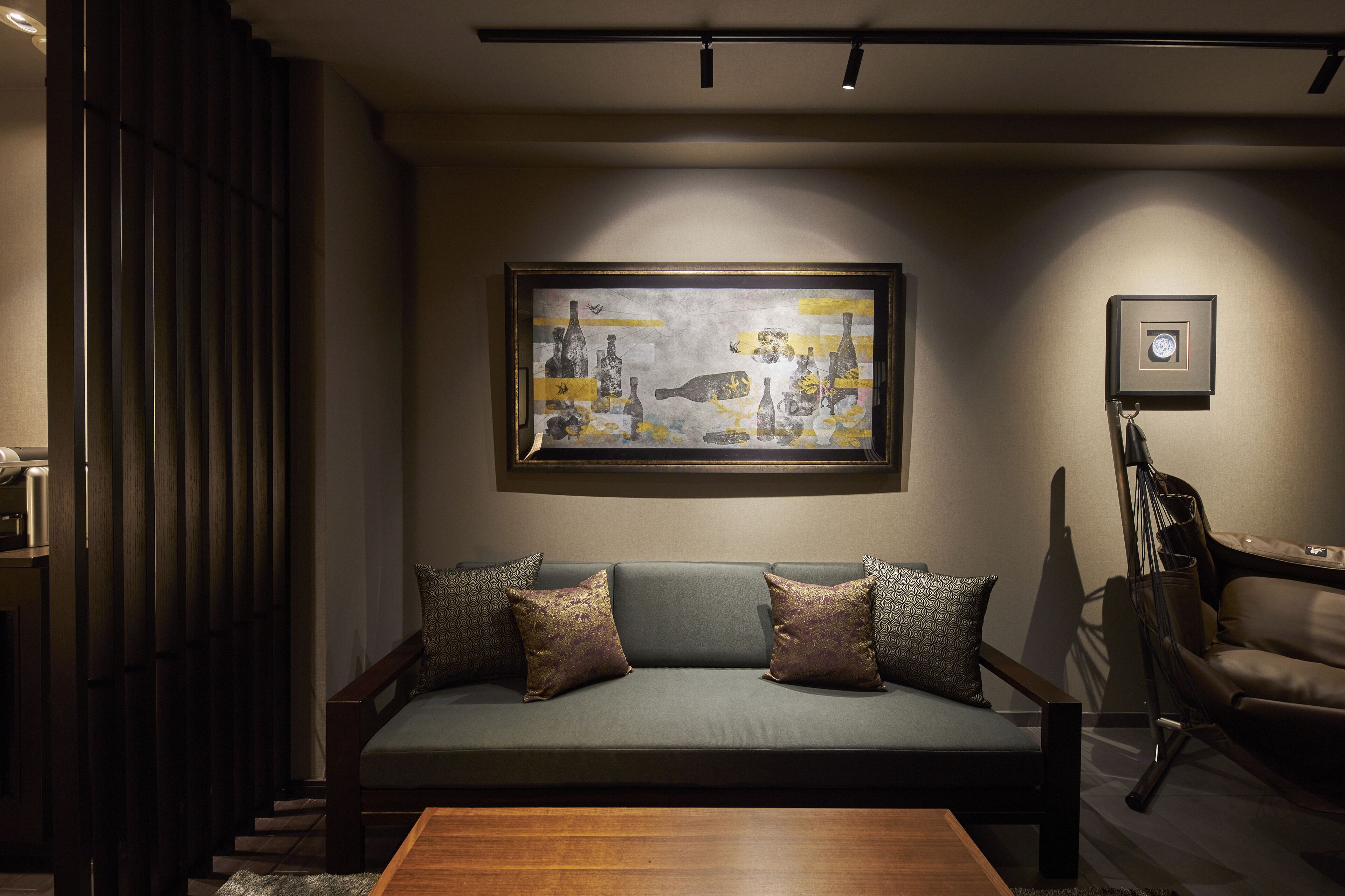 A modern living room with a grey sofa, two patterned cushions, a wooden coffee table, and a large framed artwork on the wall.