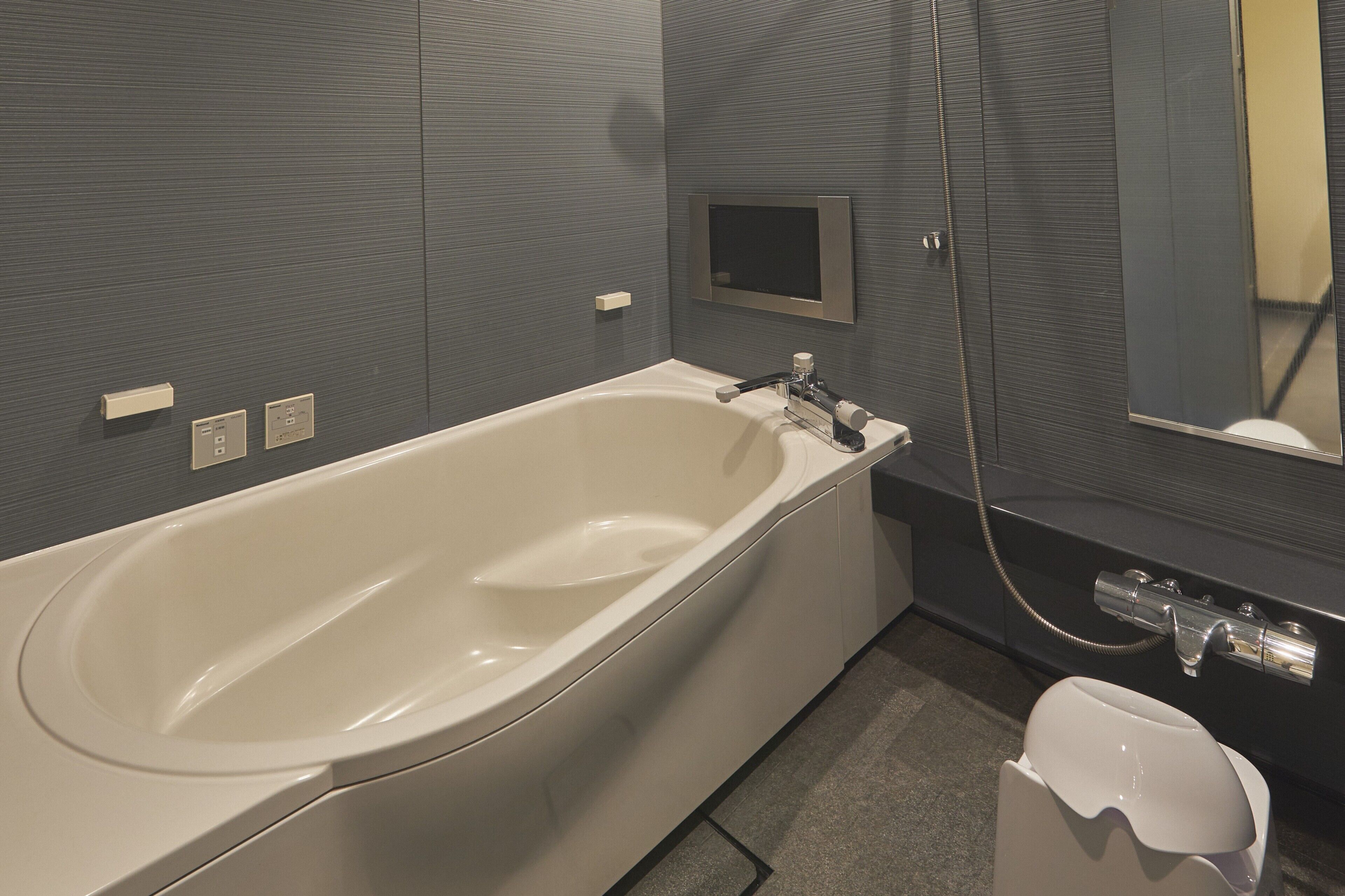 A modern bathroom with a bathtub, a toilet, a mirror, and a wall-mounted TV.