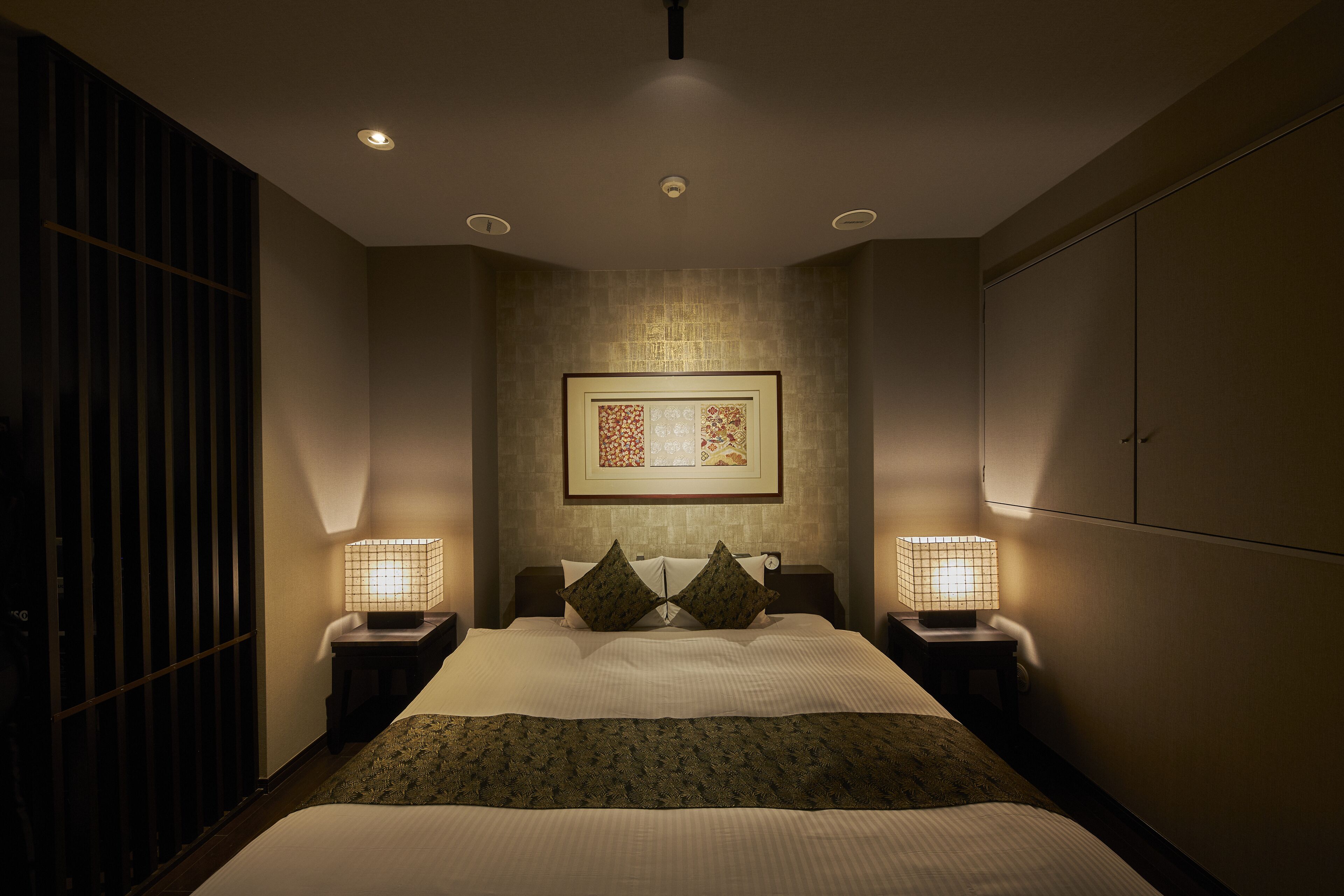 A neatly arranged bedroom with a large bed, two bedside lamps, a framed artwork on the wall, and a wardrobe.