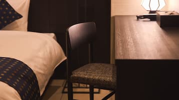 Quarto de hotel com cama, poltrona, escrivaninha e abajur.