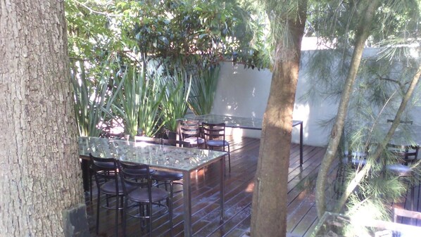 An outdoor patio with a glass table and chairs, surrounded by trees and plants. - Casa Tepoztlán (Tepoztlán)