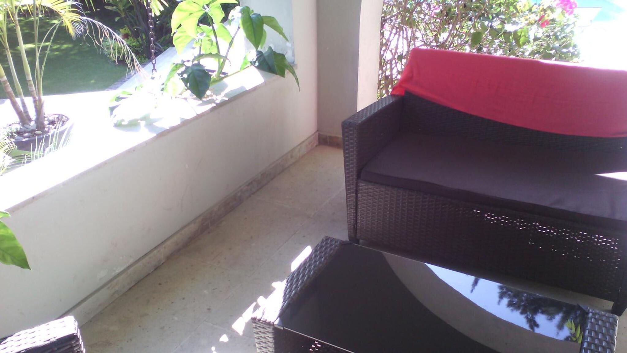 A balcony with a wicker chair and a small table, surrounded by potted plants and a view of greenery.