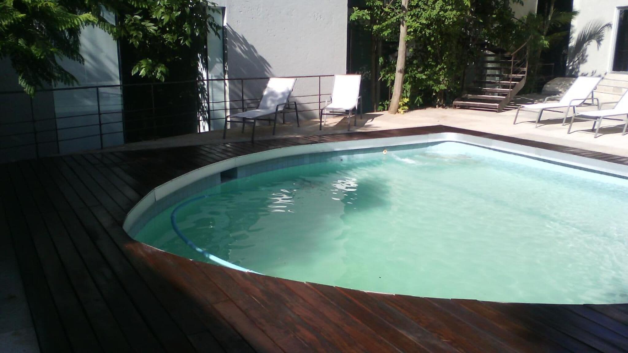 Une piscine rectangulaire entourée d’une terrasse en bois, agrémentée de chaises longues blanches et d’un escalier menant à un niveau supérieur.