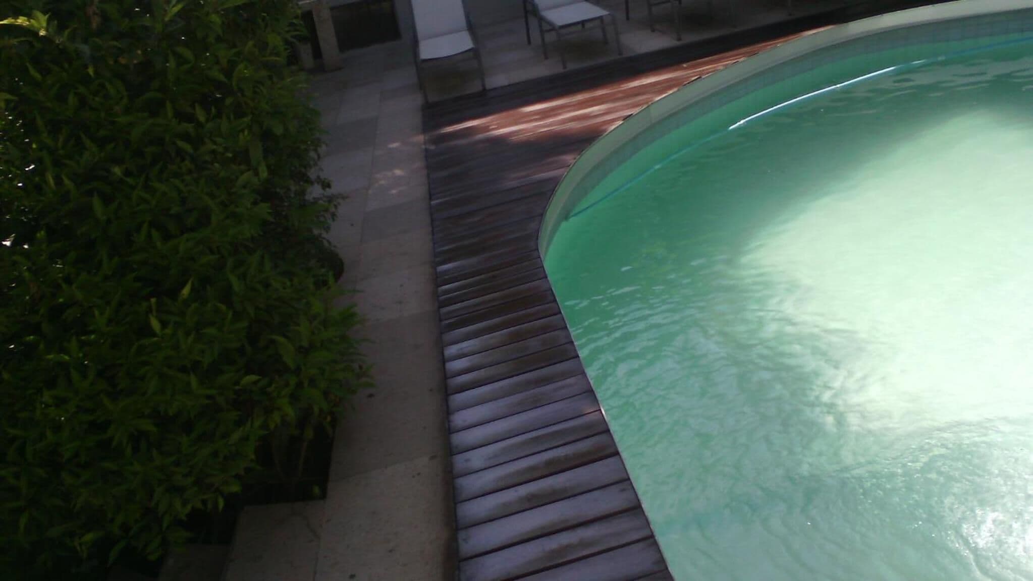 A pool area with a wooden deck and a greenish pool.