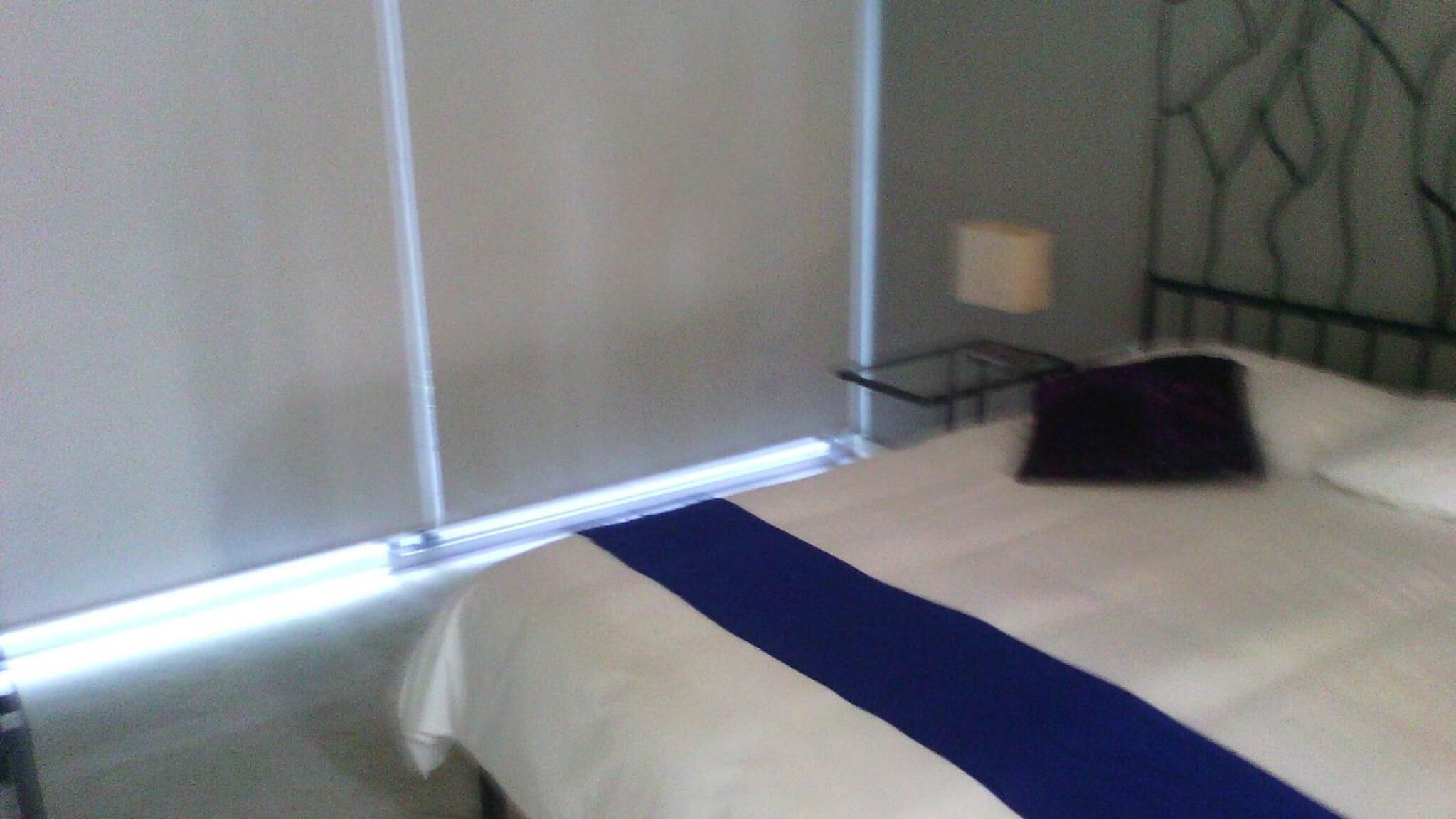 A hotel room with a bed, a nightstand, and a window with blinds.